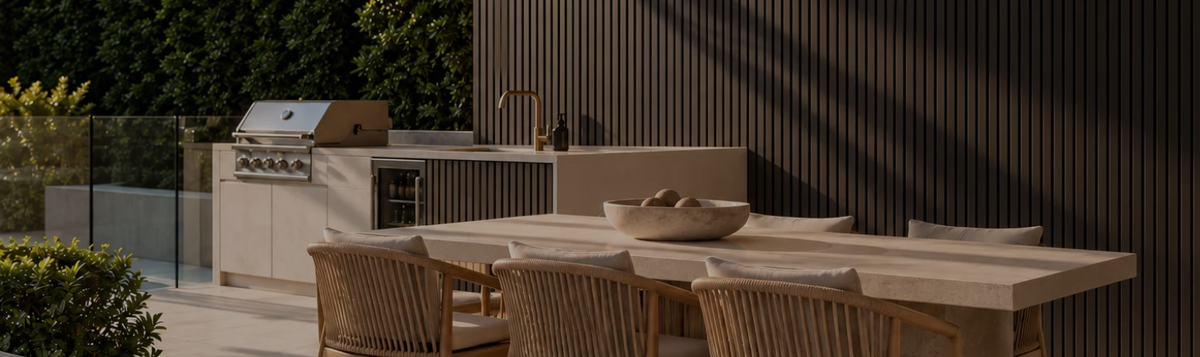 Alfresco outdoor kitchen and timber dining table in front of a black outdoor slat feature wall with a built-in barbecue